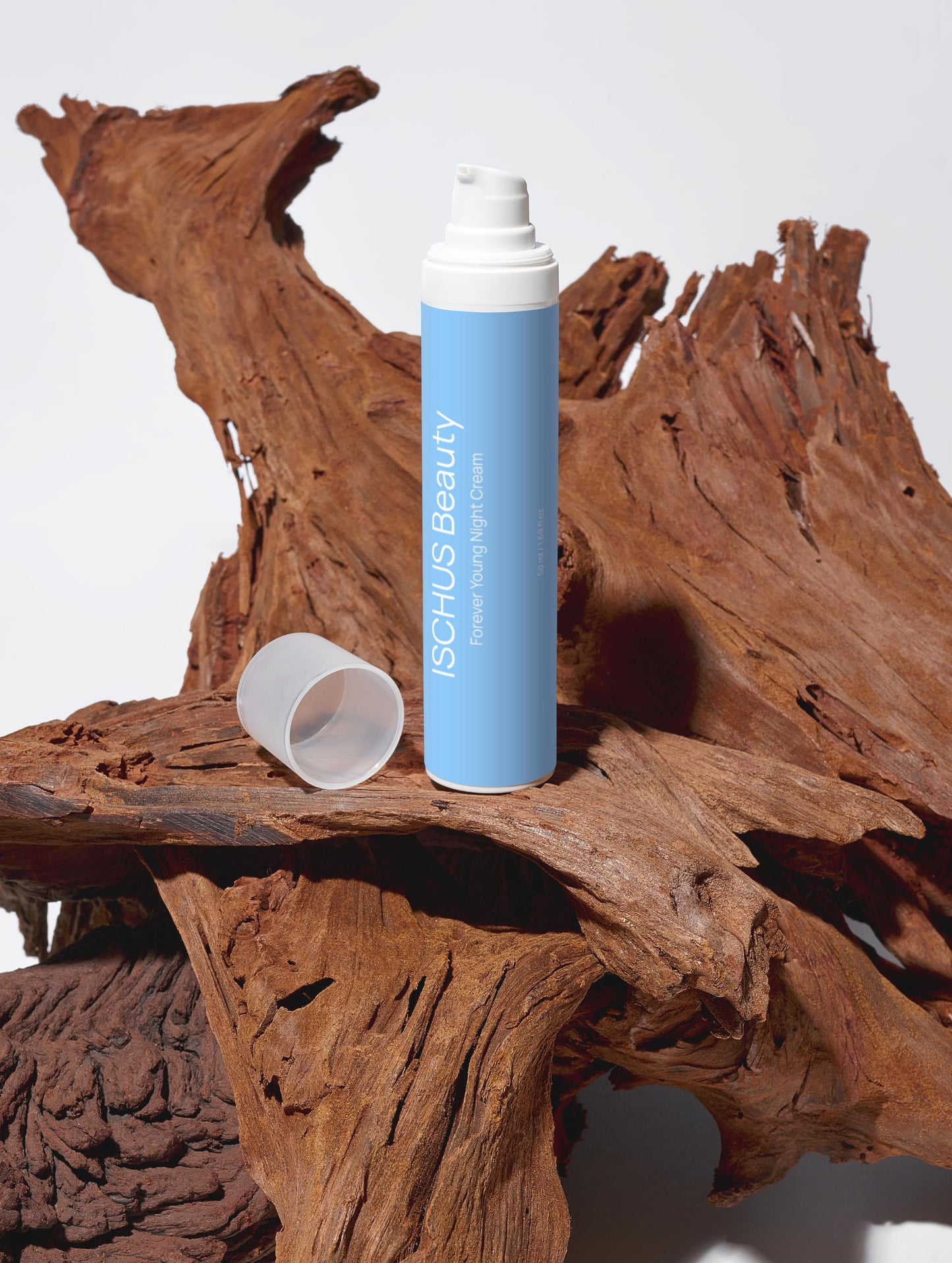 A blue bottle of Forever Young Night Cream with a white cap rests on textured brown driftwood, emphasizing its anti-aging skincare formula enriched with marine plankton extract. The white cap is placed beside the upright bottle.