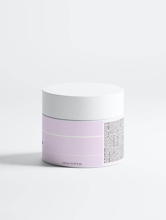 A round, light purple Nordic Volcano Face & Body Scrub jar with a white lid sits on a plain white surface. The jar displays small black text, white horizontal stripes, and "170 ml / 5.75 fl oz" printed near the base.