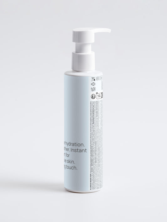 A tall, white and light blue bottle with a pump dispenser stands on a plain white background. The label reads "The Comfort Cream - Sensitive Skin Body Cream," suggesting a hydrating, soothing cream for sensitive skin.